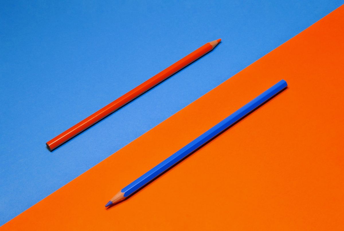 A photo of two pencils, one red, one blue juxtaposed against diagonally split red and blue background