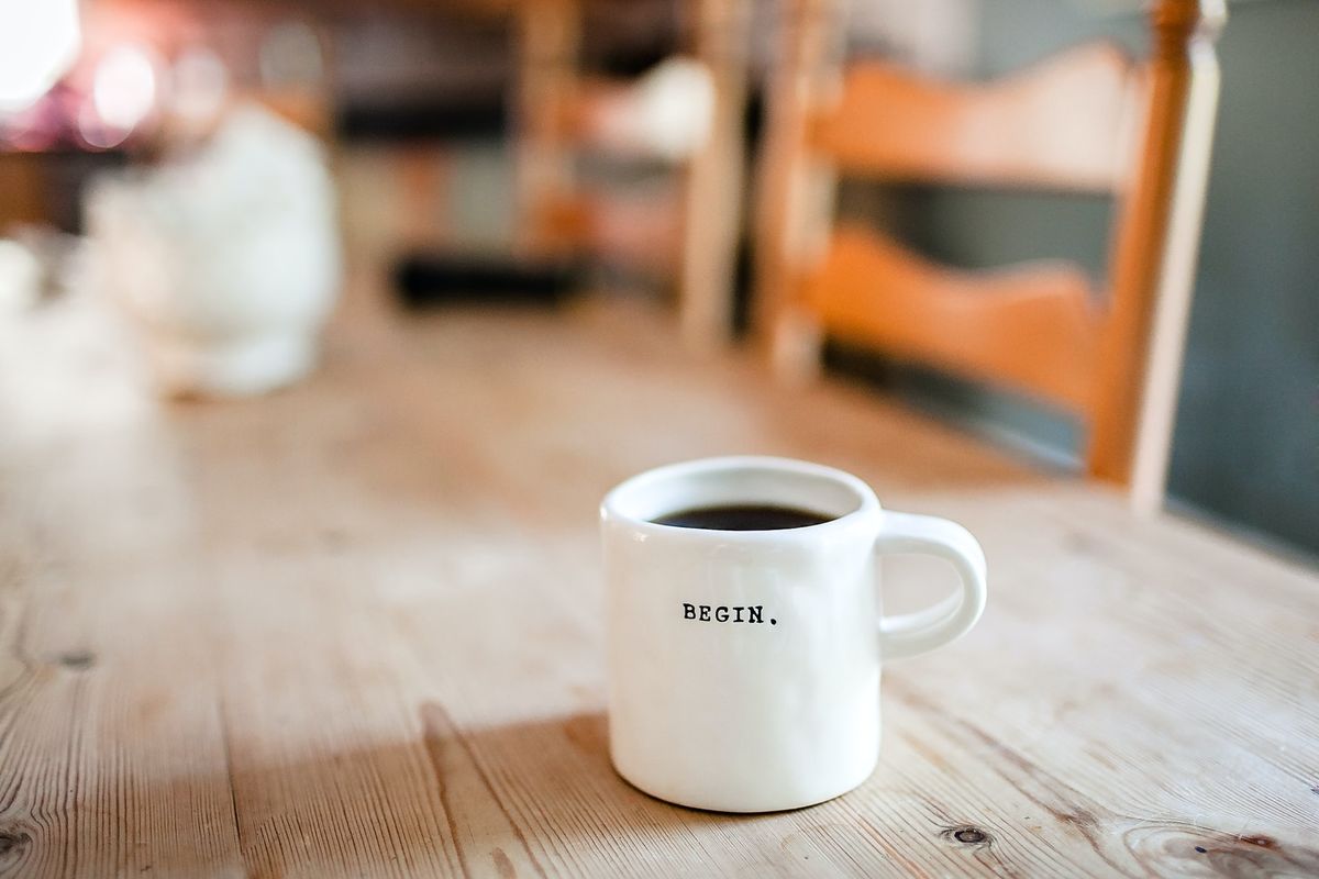 A photo of a coffee mug with the word "BEGIN" printed on it sitting on a wooden table