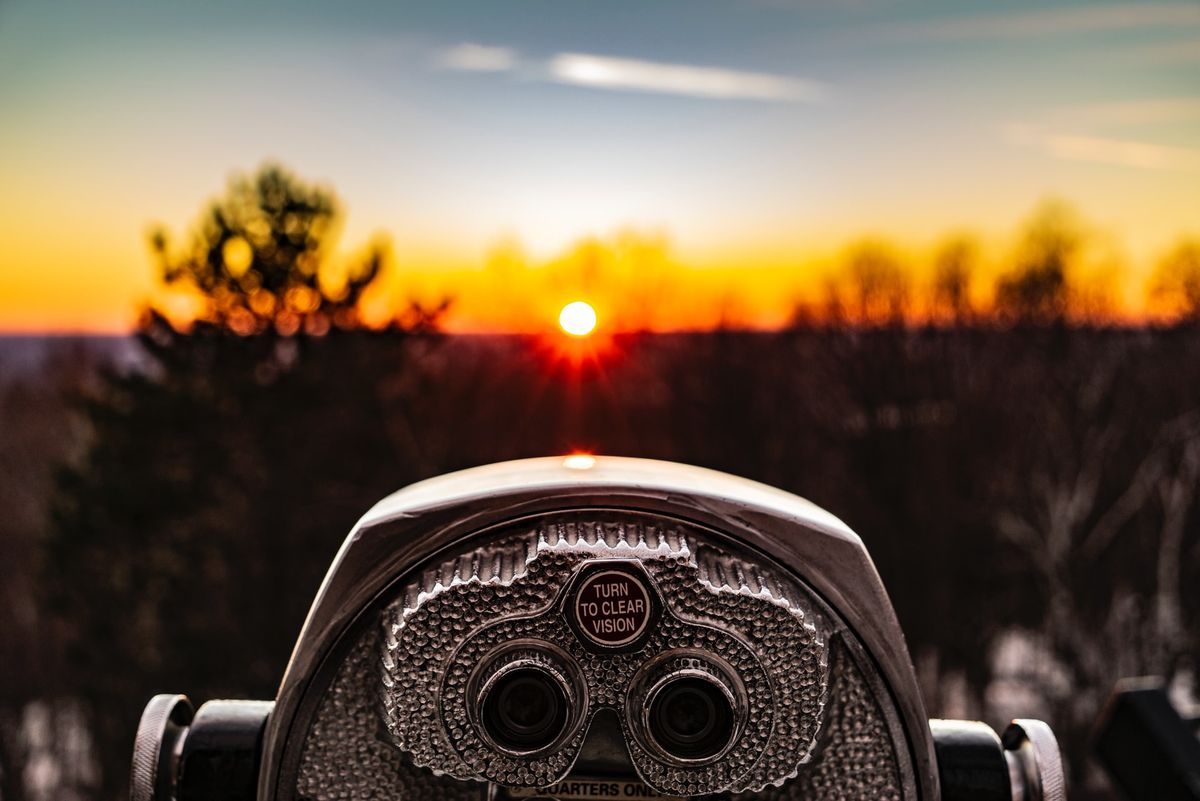 A photo of a sunset or sunrise in the background and a viewing scope in the foreground