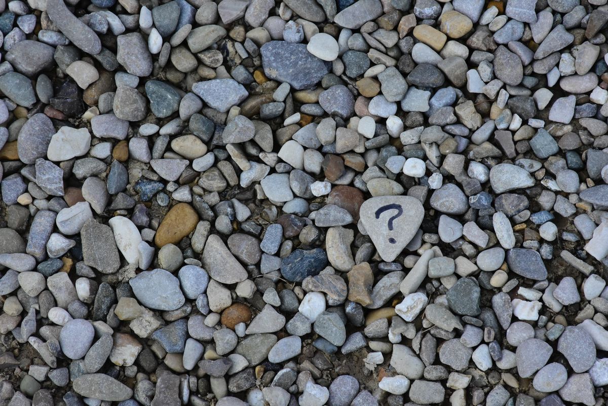 A photo of small stones, one with a question mark drawn on it