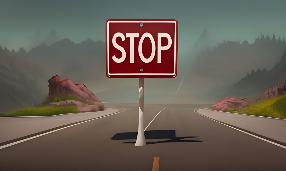 A red rectangle stop sign in the center of a road, mountains in the distance, green grass and rocks in the foreground